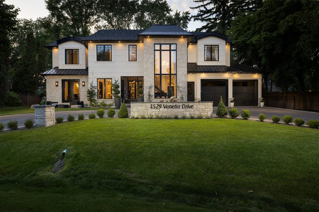 The estate's lit facade at twilight, framed by a manicured lawn and the engraved address wall