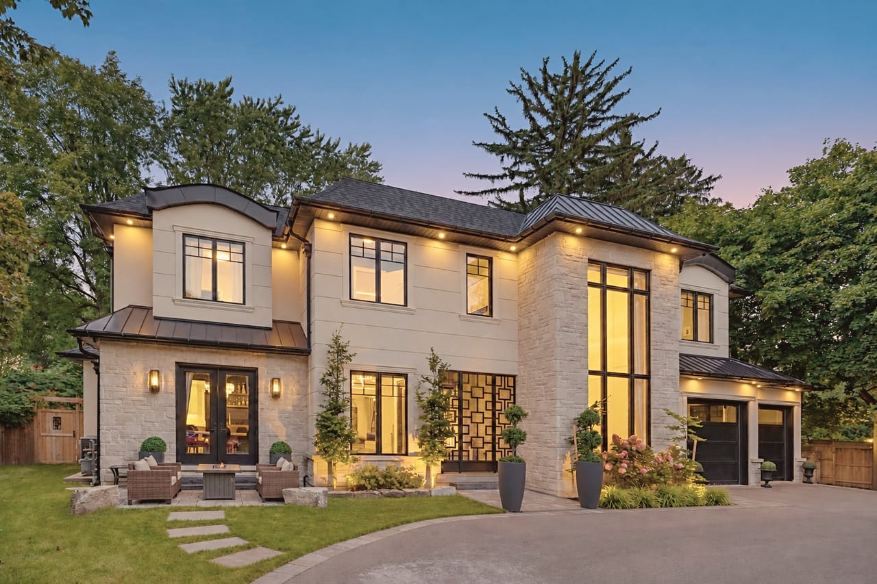 The estate at dusk from the side of the circular drive, soffit lighting tracing the rooflines
