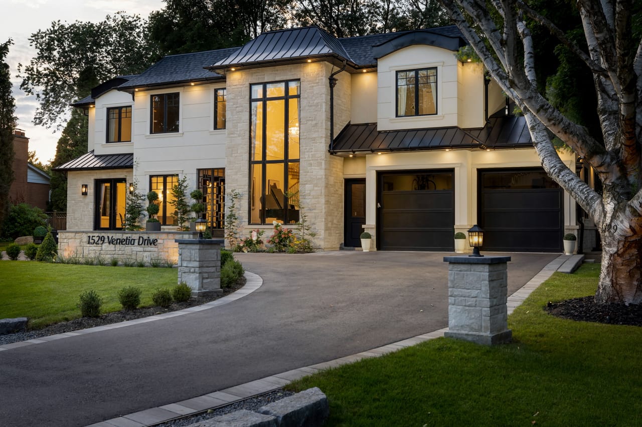 Driveway approach at dusk, stone pillars and lantern-lit garage doors along the circular drive