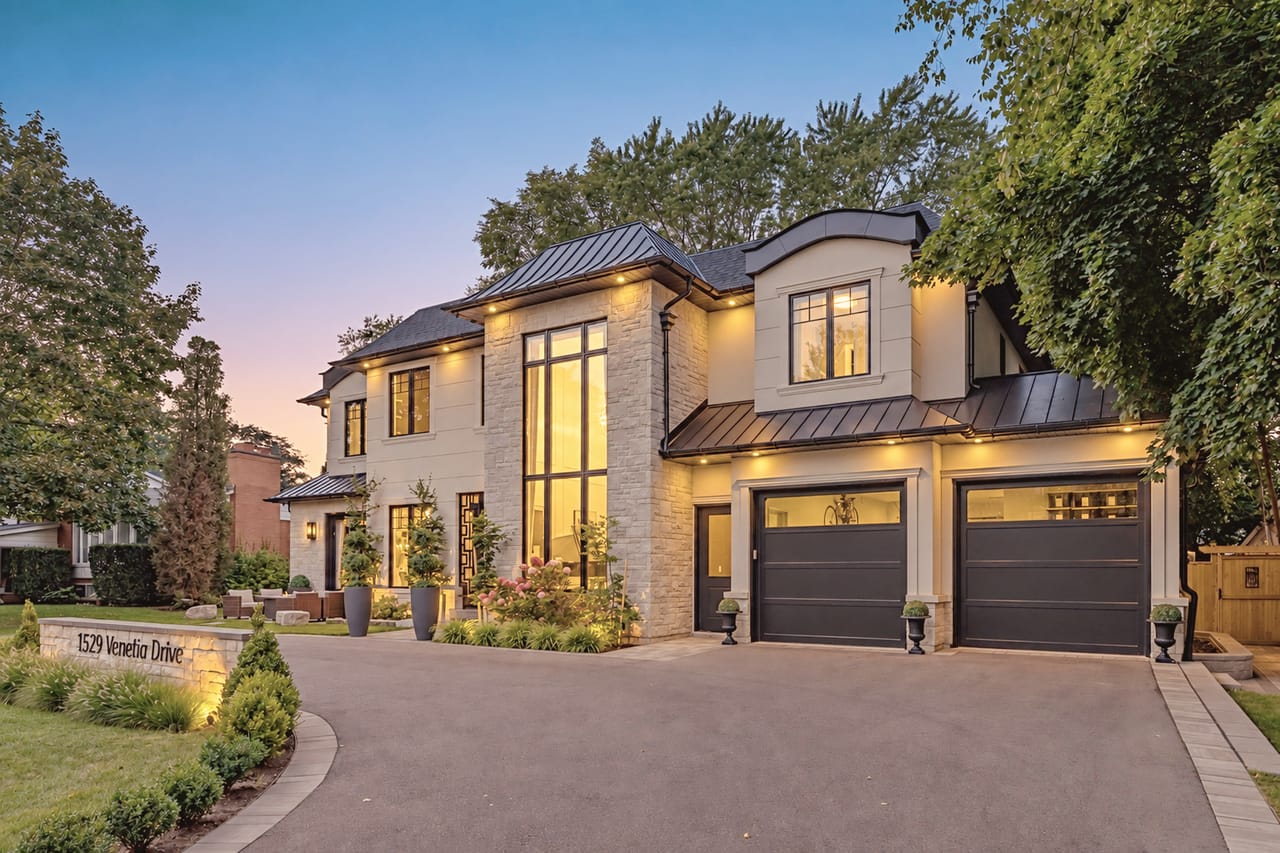 Evening approach up the driveway, garage bays and entry glowing under a pink and violet sky
