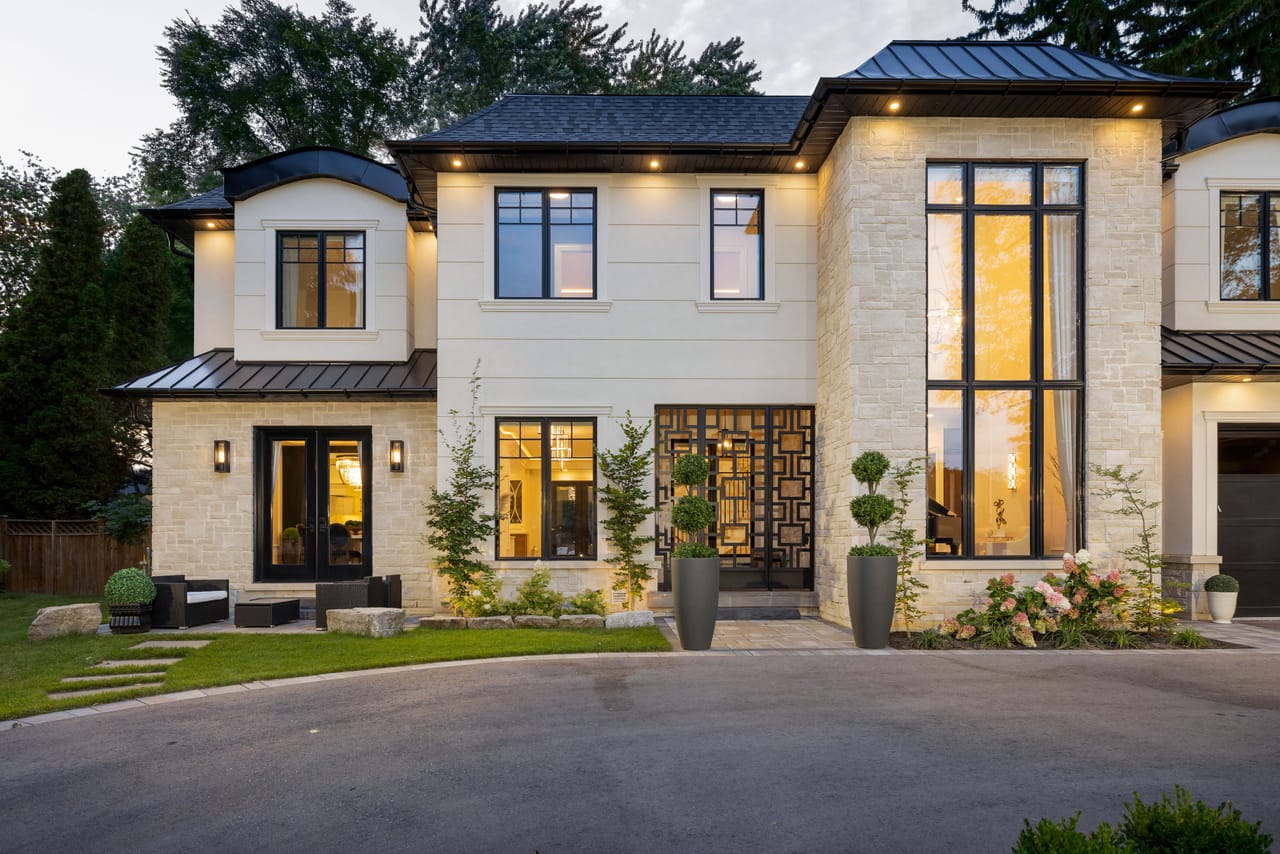 Evening view of the front entry wing, with a sculptural metal screen door and double-height windows