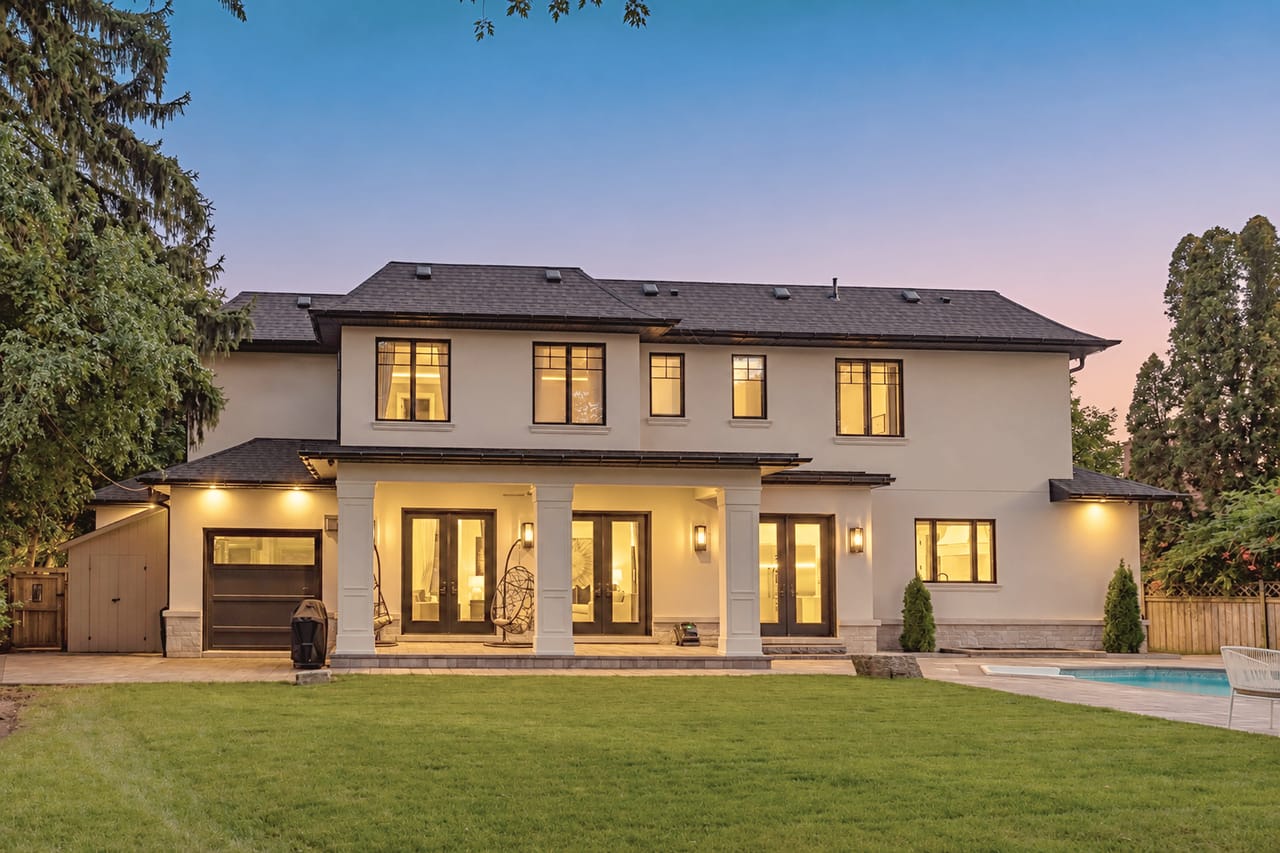 Rear elevation at dusk, the covered loggia and lit interiors overlooking the lawn