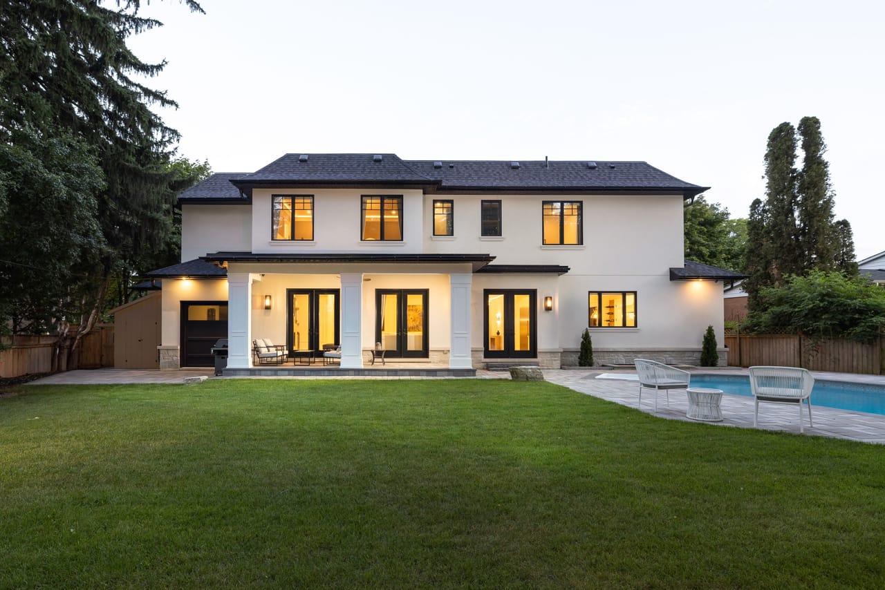 Rear elevation at dusk with a covered loggia, level lawn, and the in-ground pool