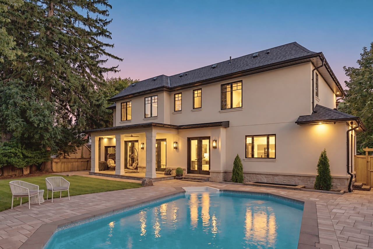 The back of the home at twilight, warm windows reflected in the pool