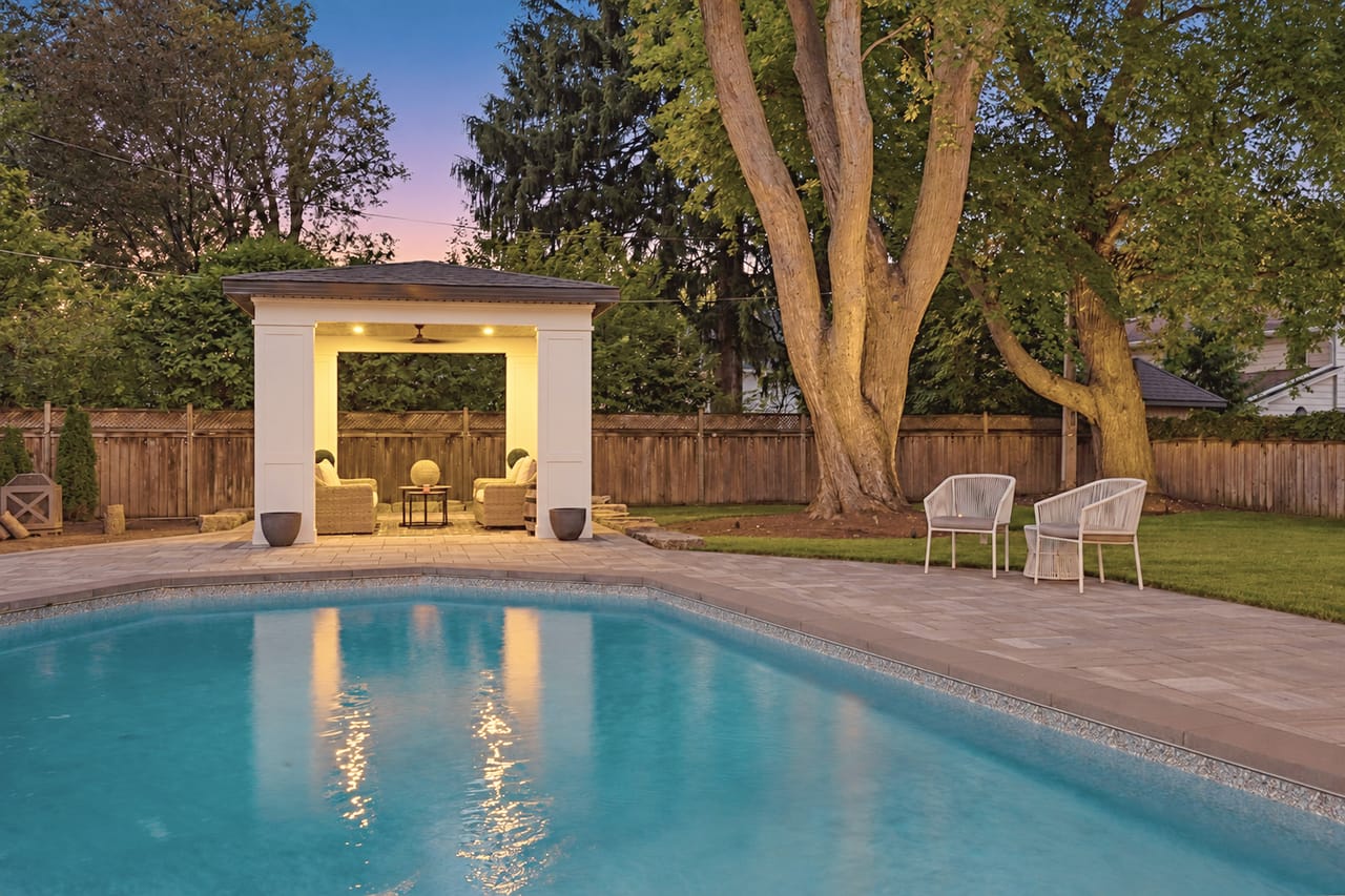 The pool at dusk, mirror still, with the cabana lit beneath mature trees