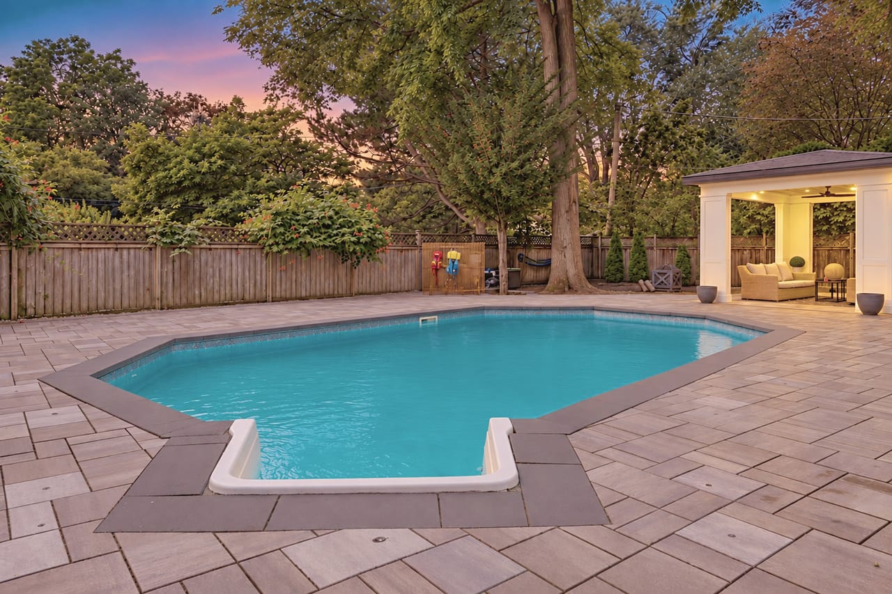 Poolside at nightfall, the open cabana glowing under a canopy of old maples