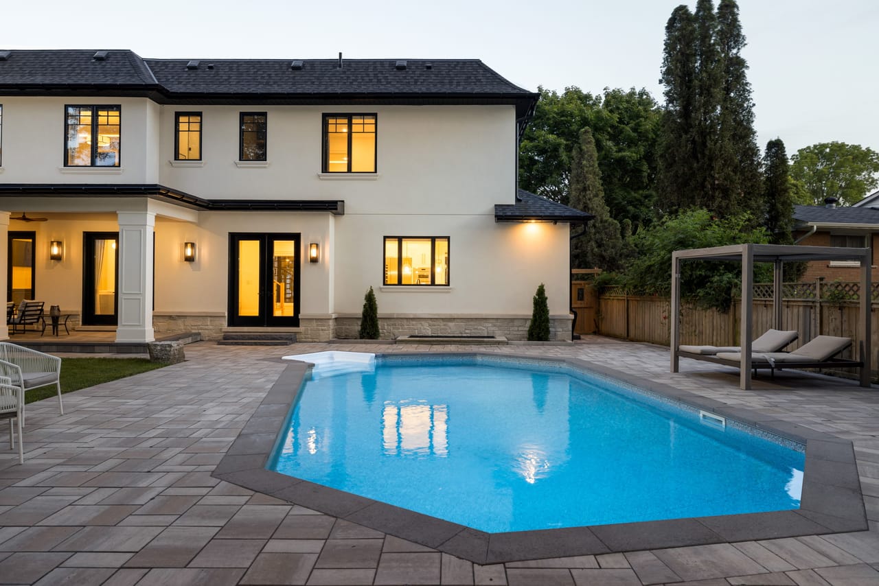 Illuminated rear of the home at dusk, glowing interiors above the poolside terrace