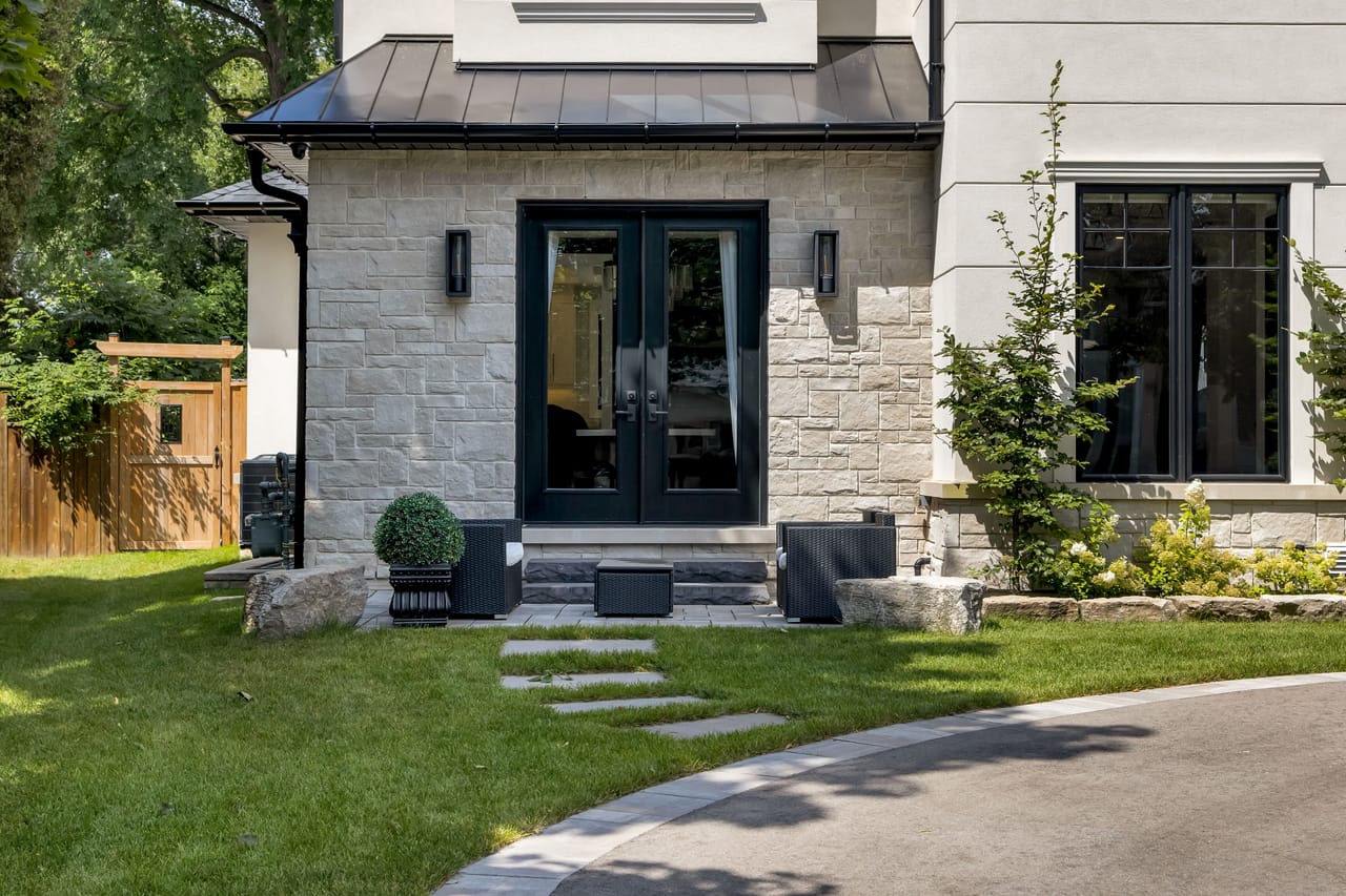 Side garden entrance with black French doors, stone walls, and a flagstone path