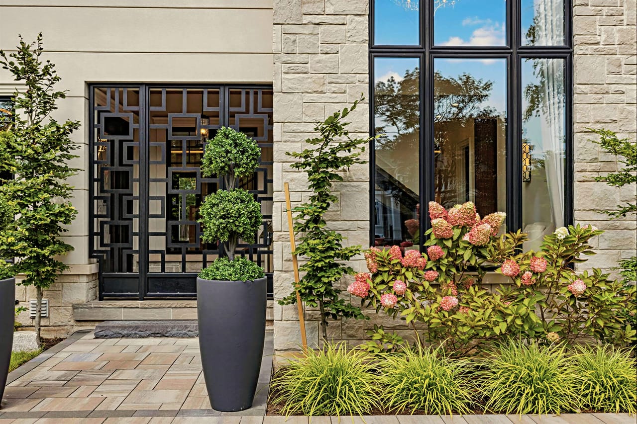 The front door screen in laser-cut steel, framed by hydrangeas and clipped topiary