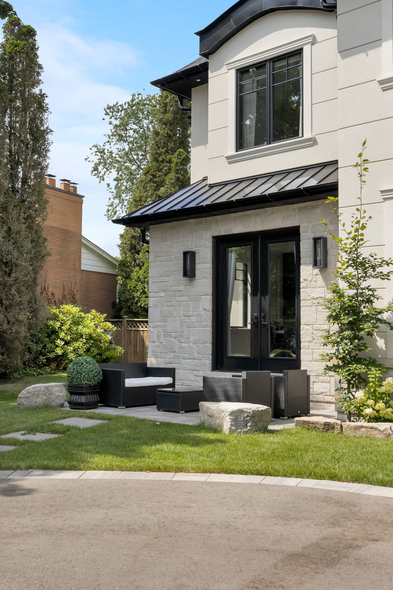 Covered side porch with stone walls, a quiet sitting nook, and garden views