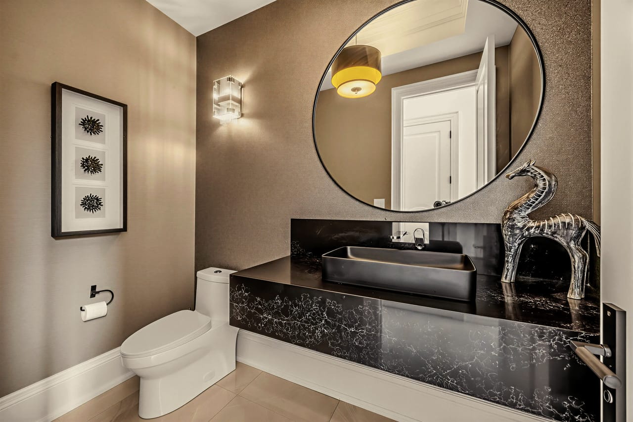 Powder room with a vessel sink on honed black stone beneath a round backlit mirror