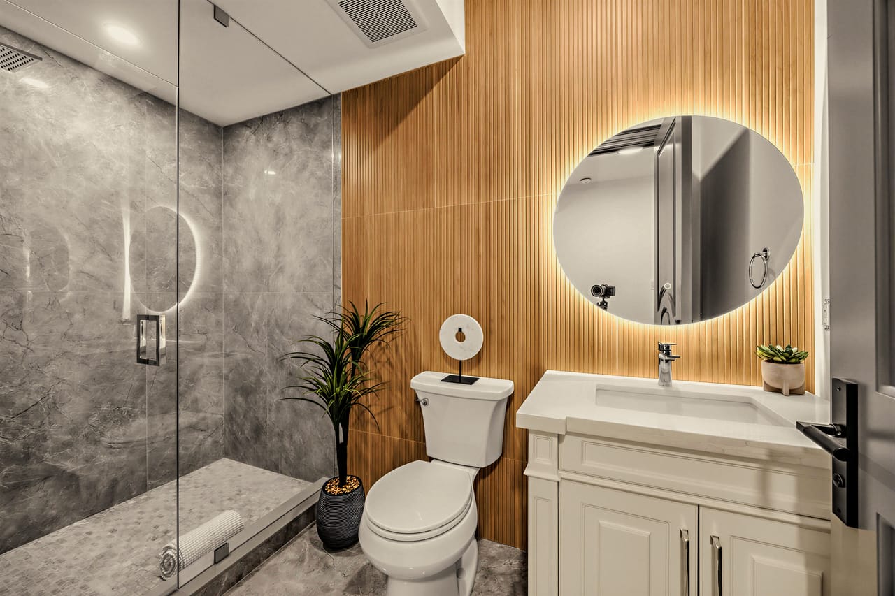 The nanny suite ensuite on the lower level, glass shower beside a warm oak slat wall