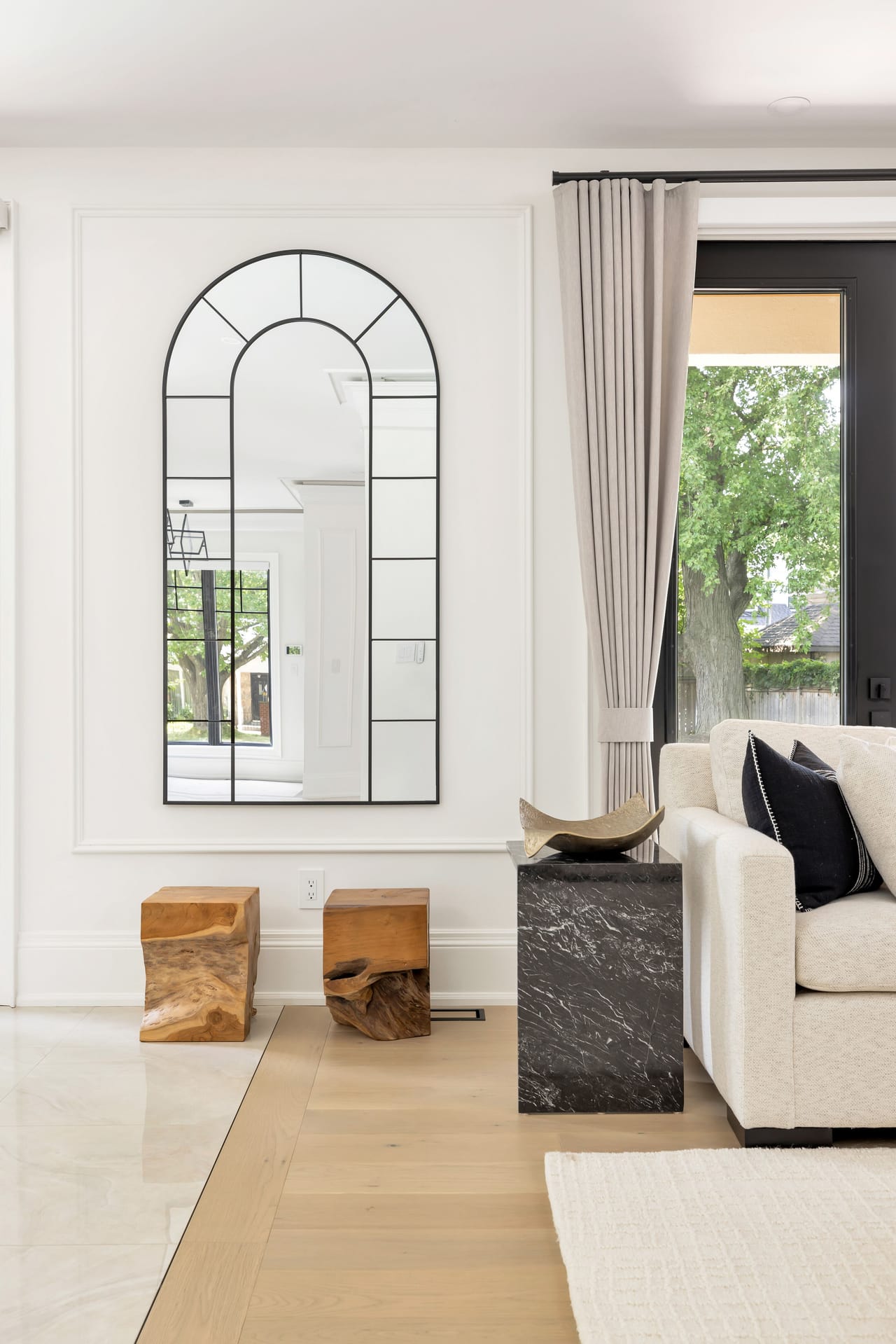 Living room corner with an arched windowpane mirror and teak side tables