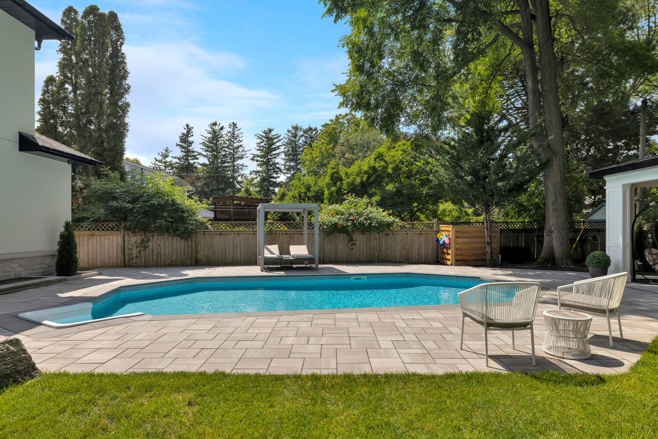 Pool and cabana in daylight, loungers on the paver deck behind a privacy fence