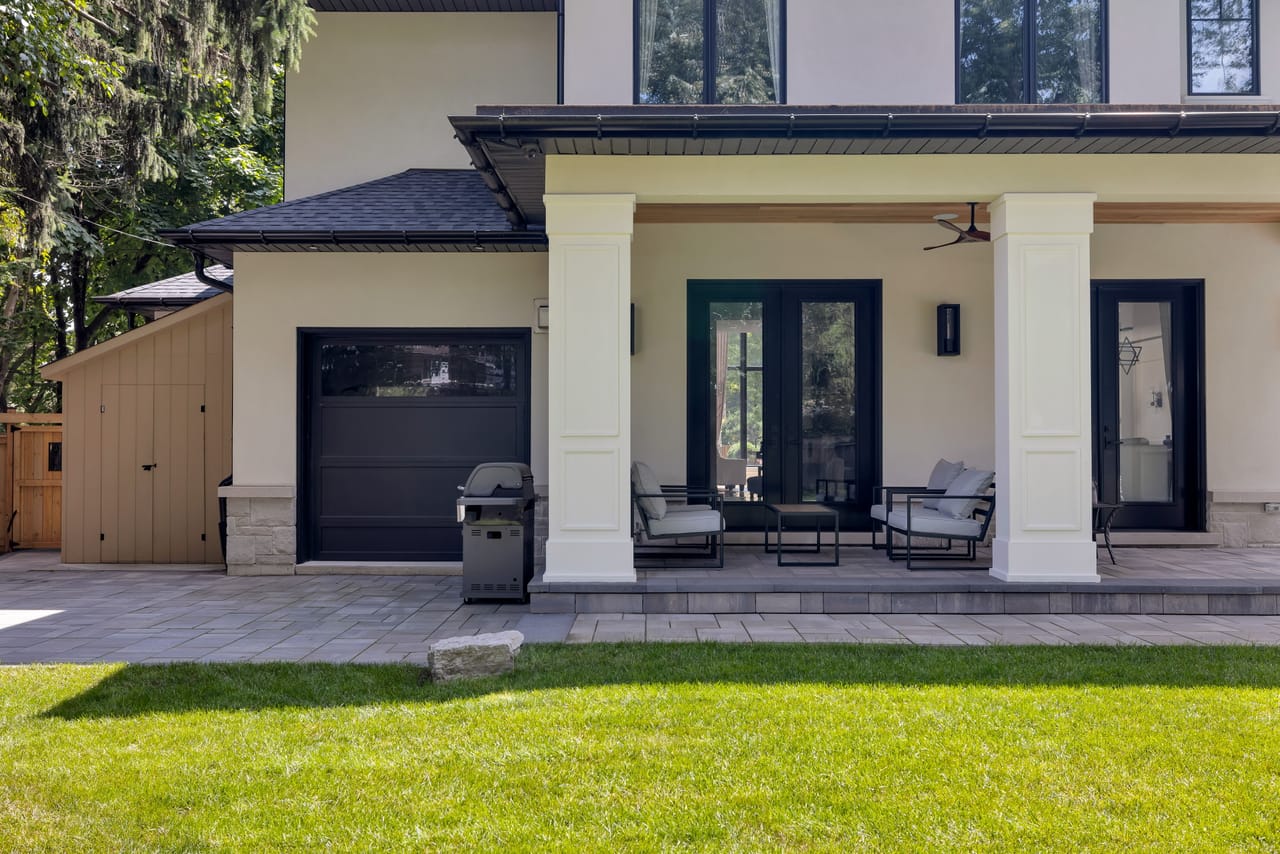 Covered rear loggia with lounge seating and a built-in grill beside the garage