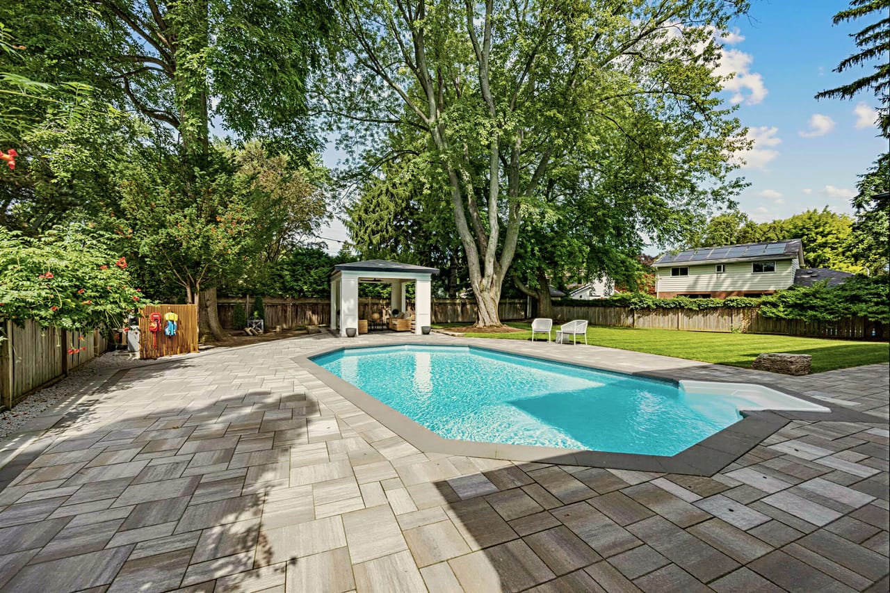 In-ground pool on the stone terrace, open cabana beyond under mature trees