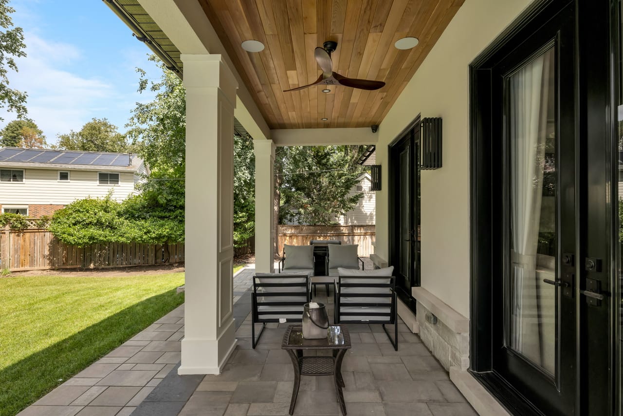 Covered loggia with a cedar-slat ceiling and lounge seating opening to the yard