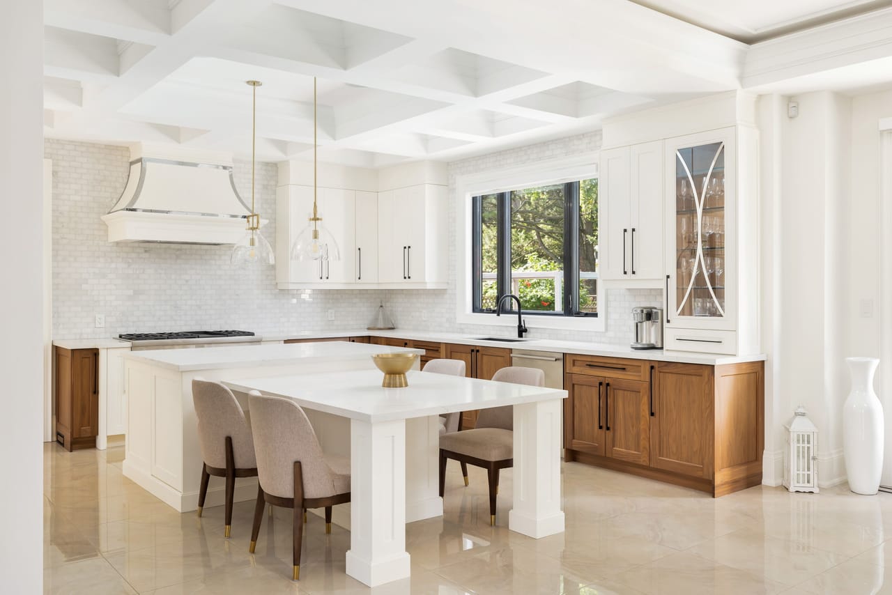 Kitchen island seating beneath a custom hood, with marble counters and a window over the sink