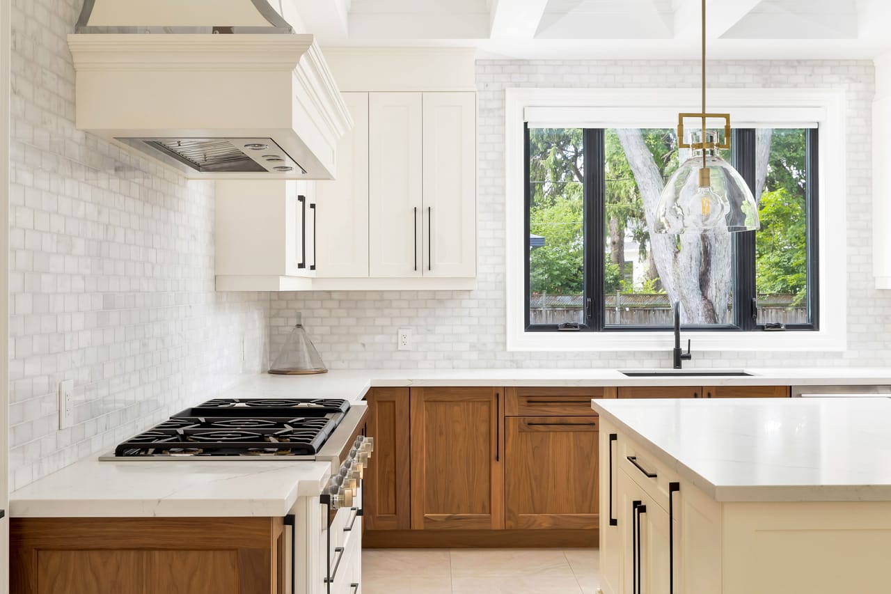Six-burner gas cooktop set in marble, framed by a herringbone backsplash and a glass pendant