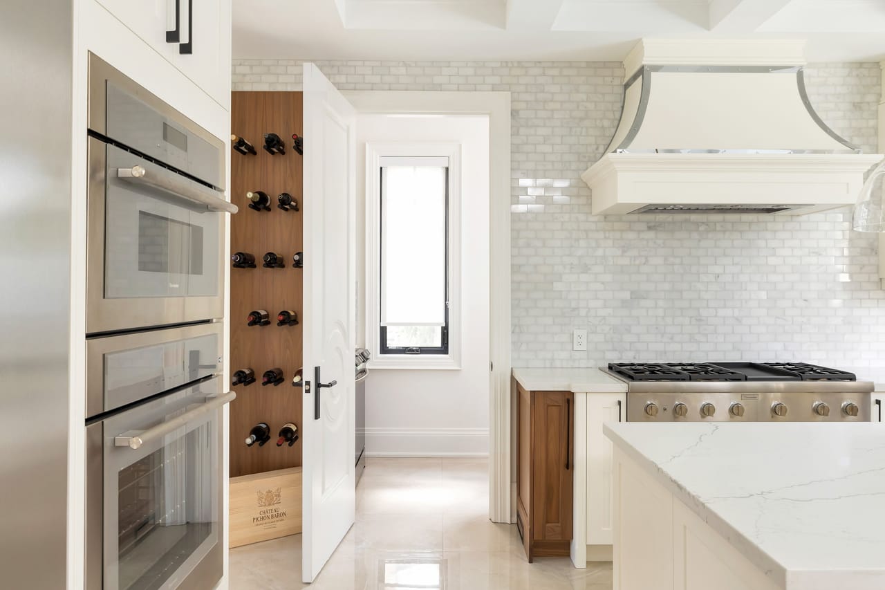 Double wall ovens and a walnut wine wall beside the range, with a passage to the working kitchen