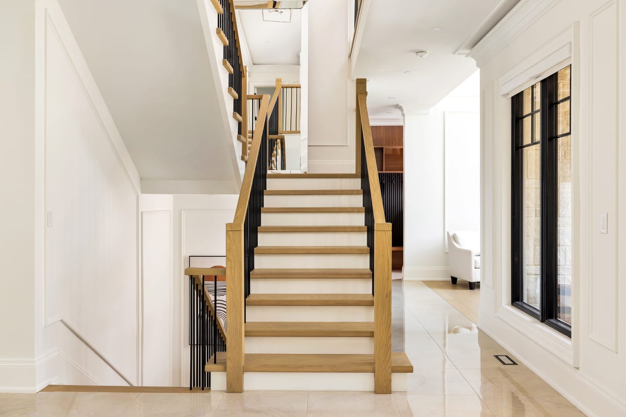 Open oak staircase with black metal balusters rising from the marble landing