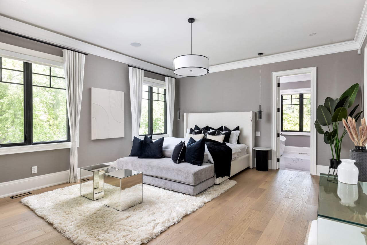 Primary bedroom in soft grey, an upholstered bed and chaise beneath a drum pendant