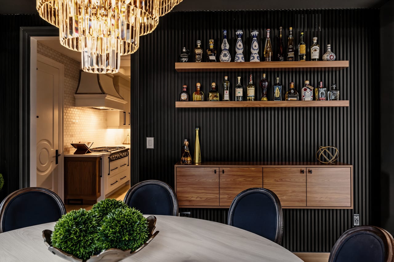 The bar wall at night, bottles lit along the oak shelves