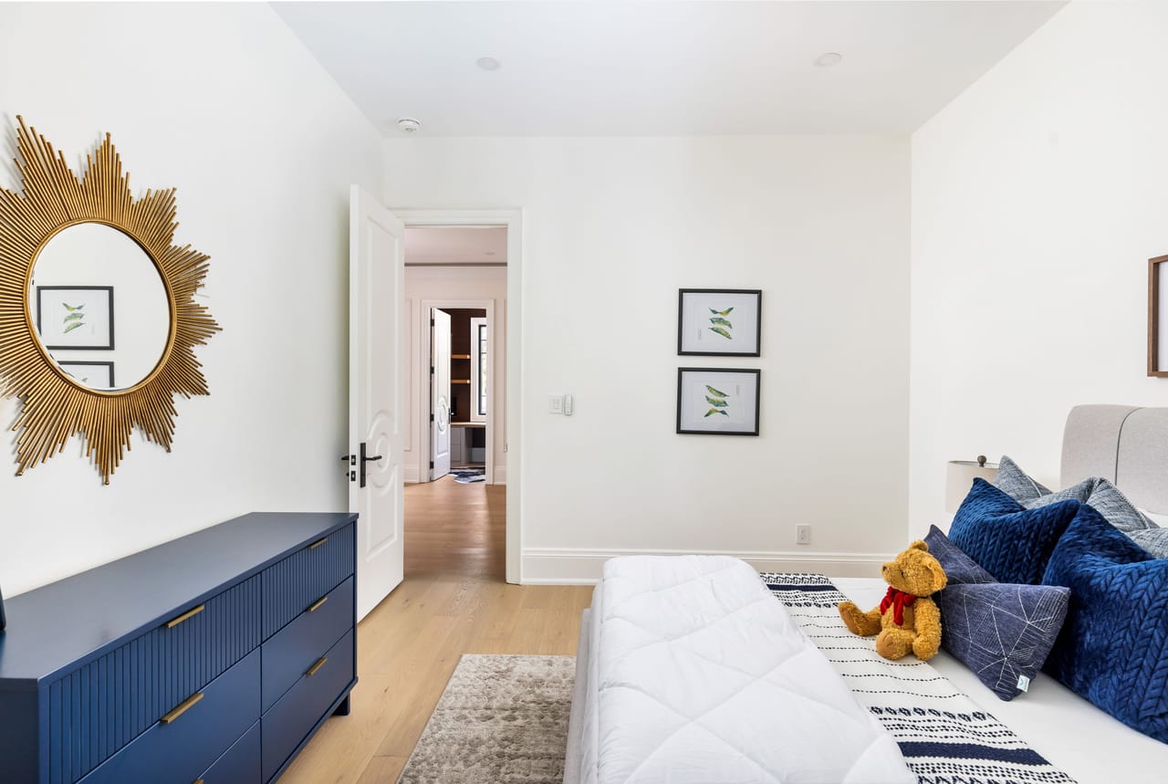 Secondary bedroom with a navy dresser, sunburst mirror, and botanical prints