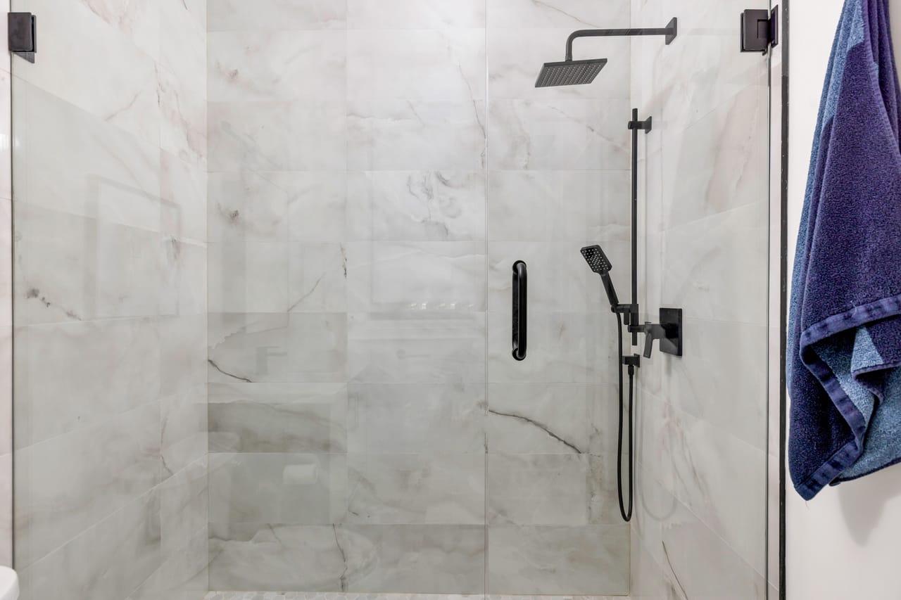 Walk-in shower clad in marble with black rainfall and handheld fixtures