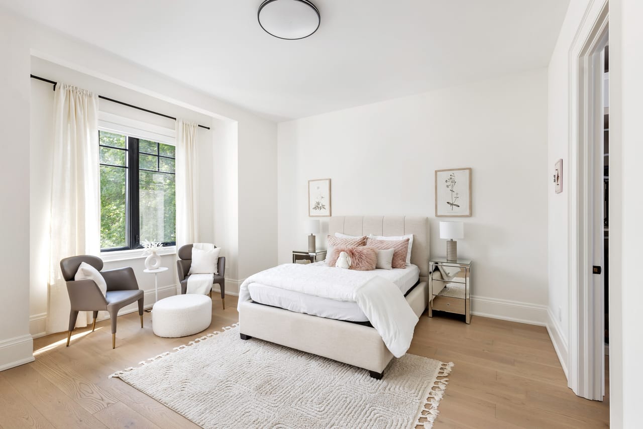 Secondary bedroom with mirrored nightstands and a quiet sitting area by the window