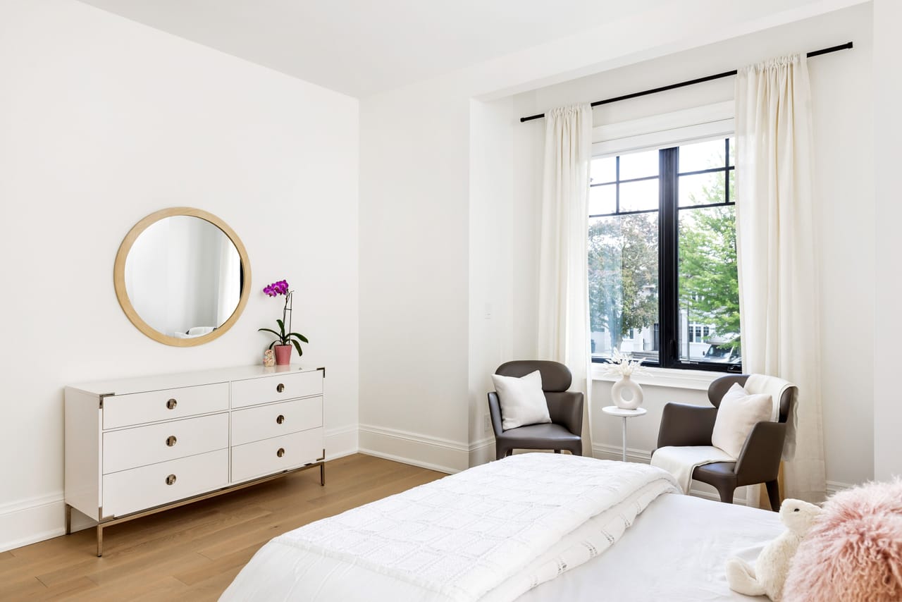 Secondary bedroom with a round mirror, paired chairs, and a tall casement window