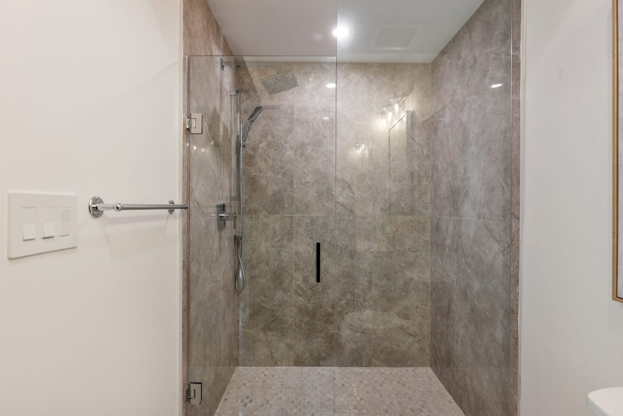 Guest shower finished in grey marble behind frameless glass