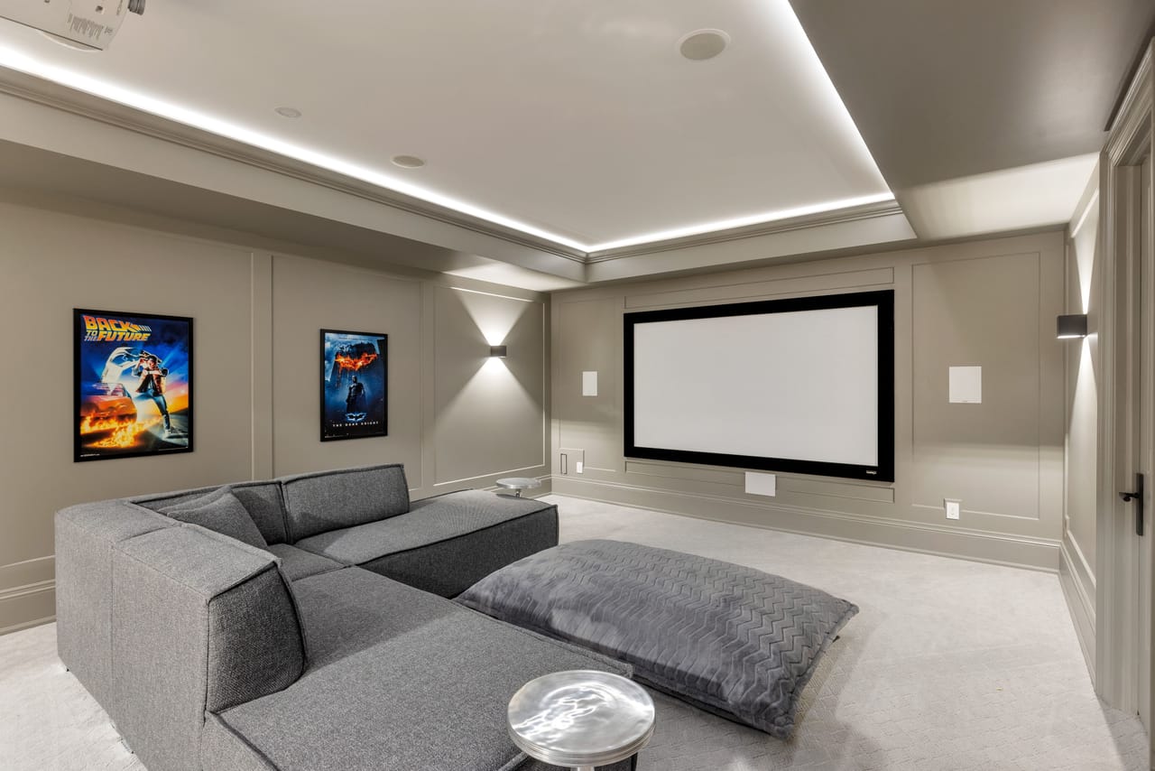Home theatre lounge beneath cove lighting, with framed film posters along the wall