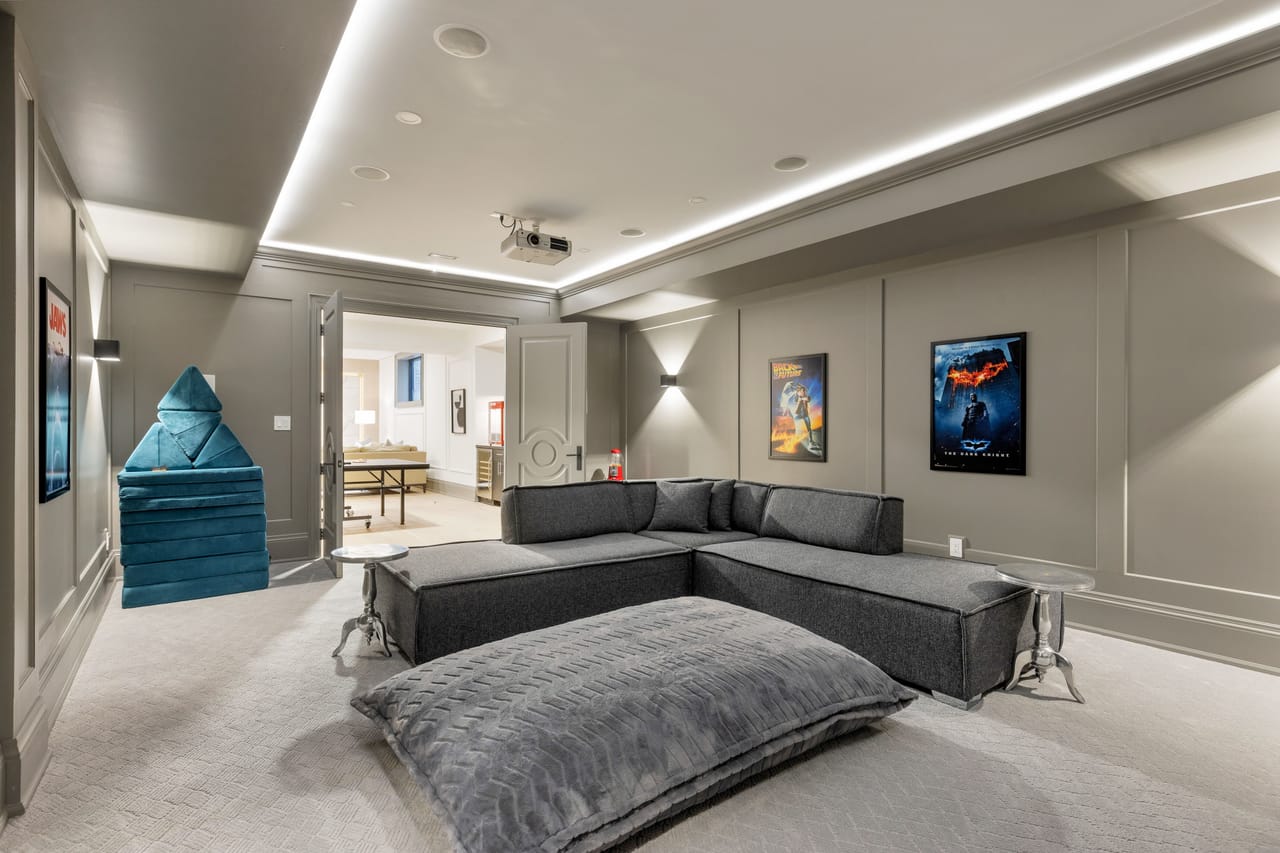 Screening room with plush seating, a projector, and a doorway to the games room