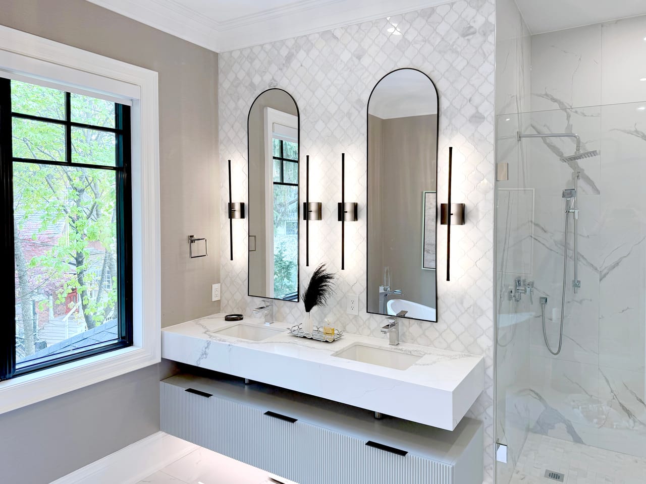 Primary ensuite double vanity beneath twin arched mirrors, beside a glass shower