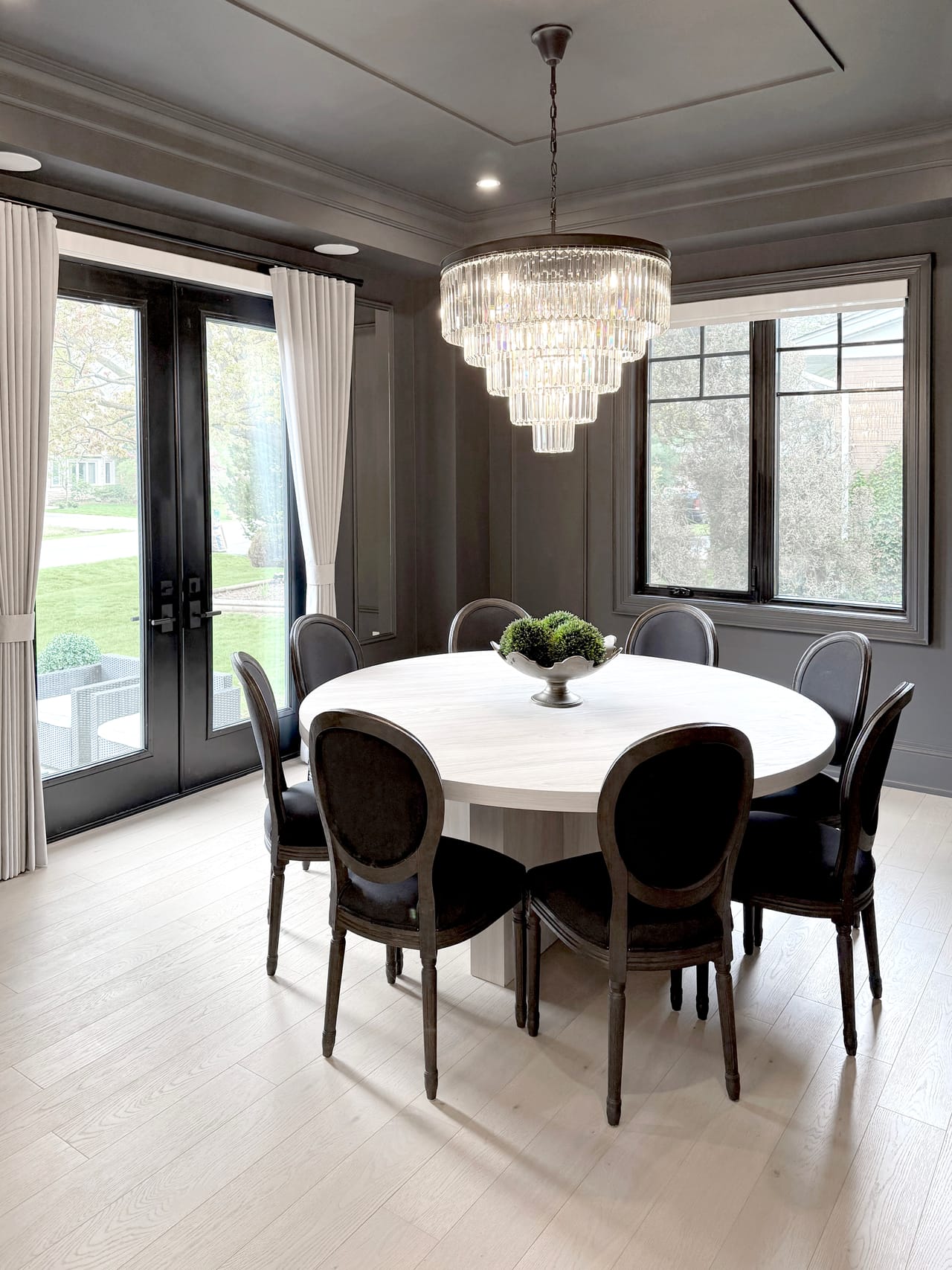 Formal dining room with a tiered crystal chandelier, a round table for eight, and garden doors