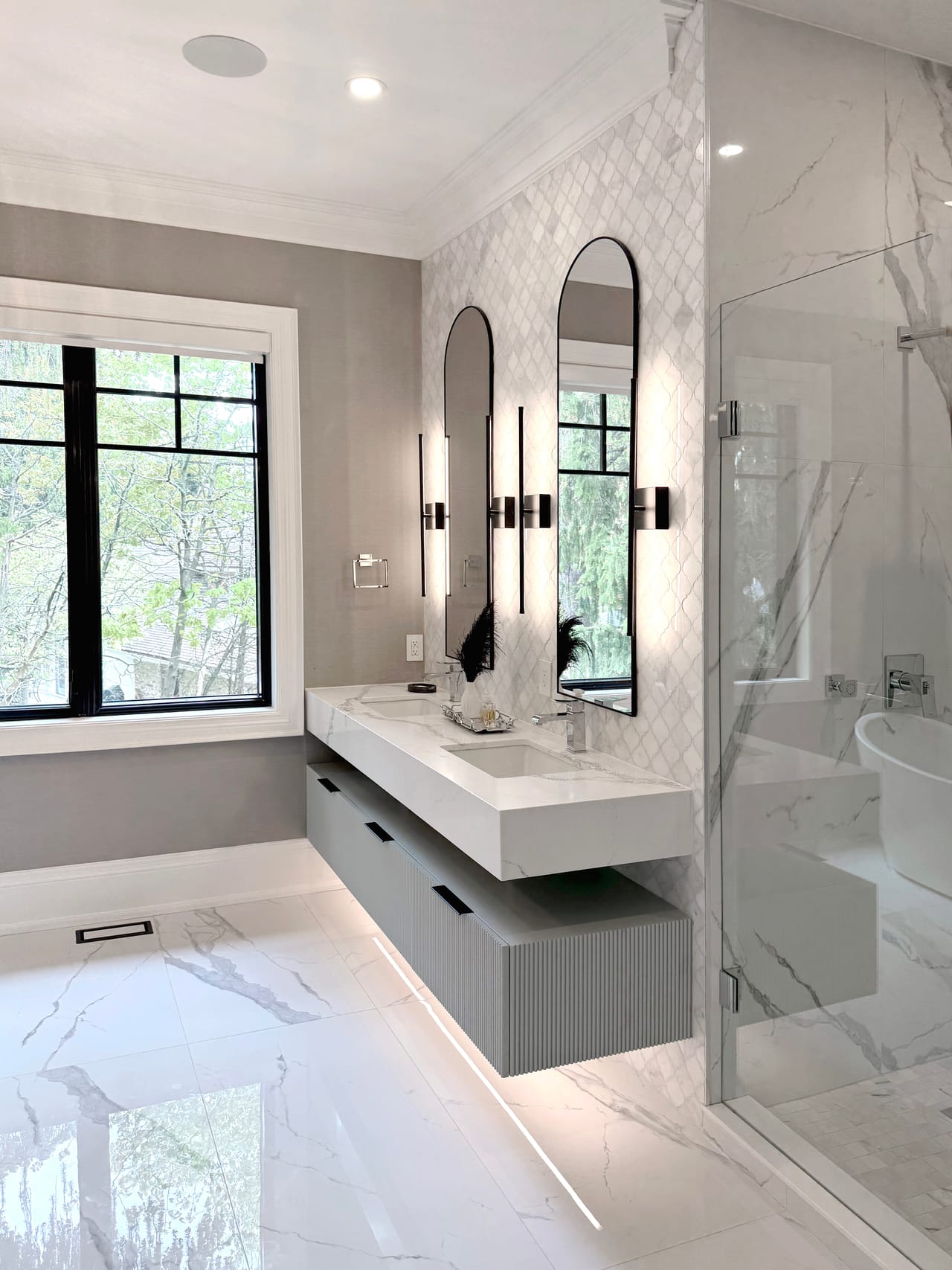 Primary ensuite with a floating double vanity, arched mirrors, and a marble feature wall